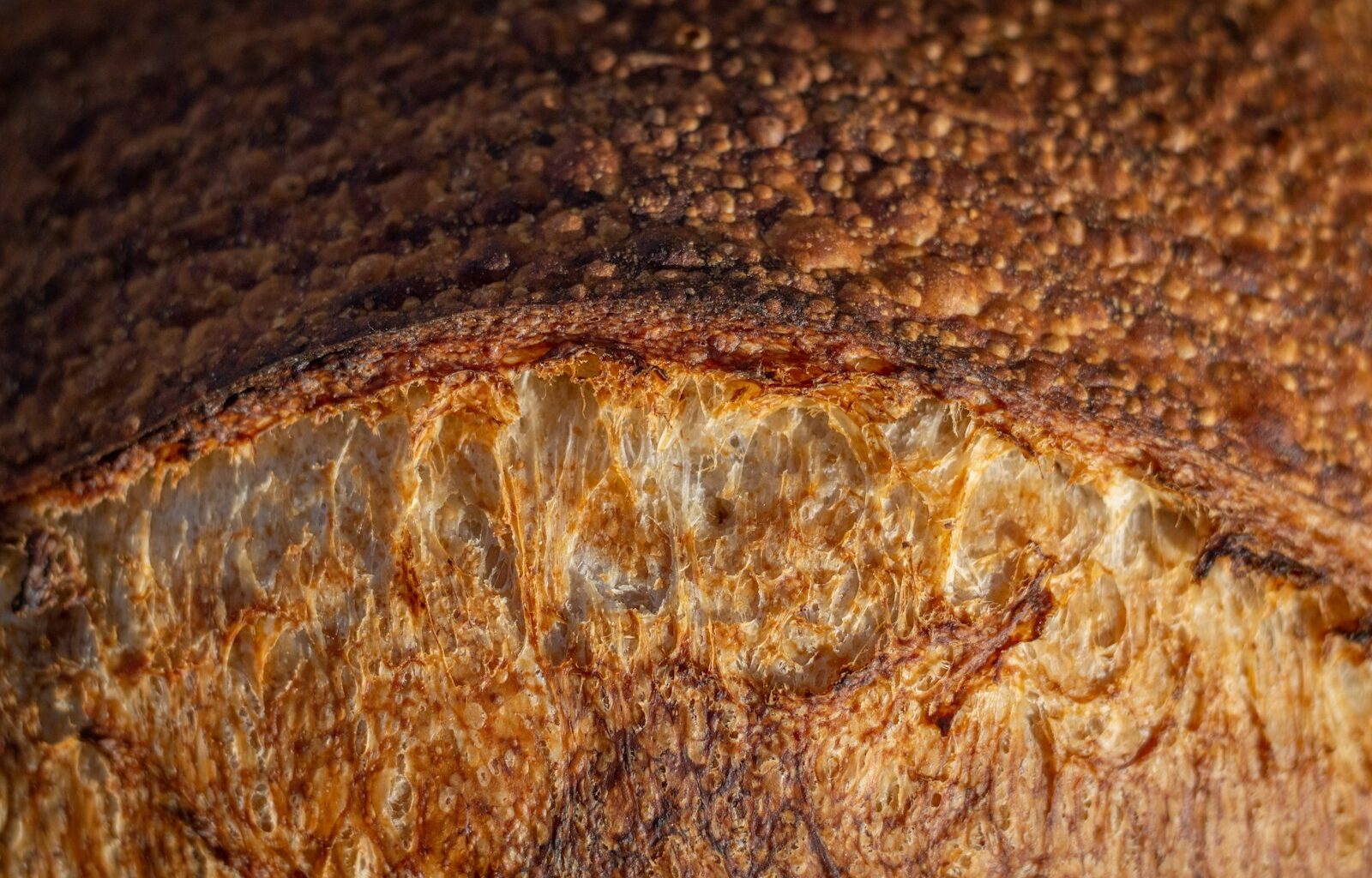 Aangesneden zuurdesembrood op een houten plank naast een linnen doek